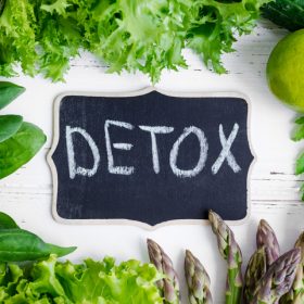 Detox concept with green vegetables: spinach, lettuce, cucumber, ginger, asparagus, broccoli and lime. White wooden background. Clean eating Vegetarian food Healthy fitness lifestyle. Top view.